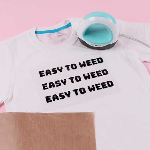 White t-shirt with 'EASY TO WEED' text, iron, and cardboard on a pink background